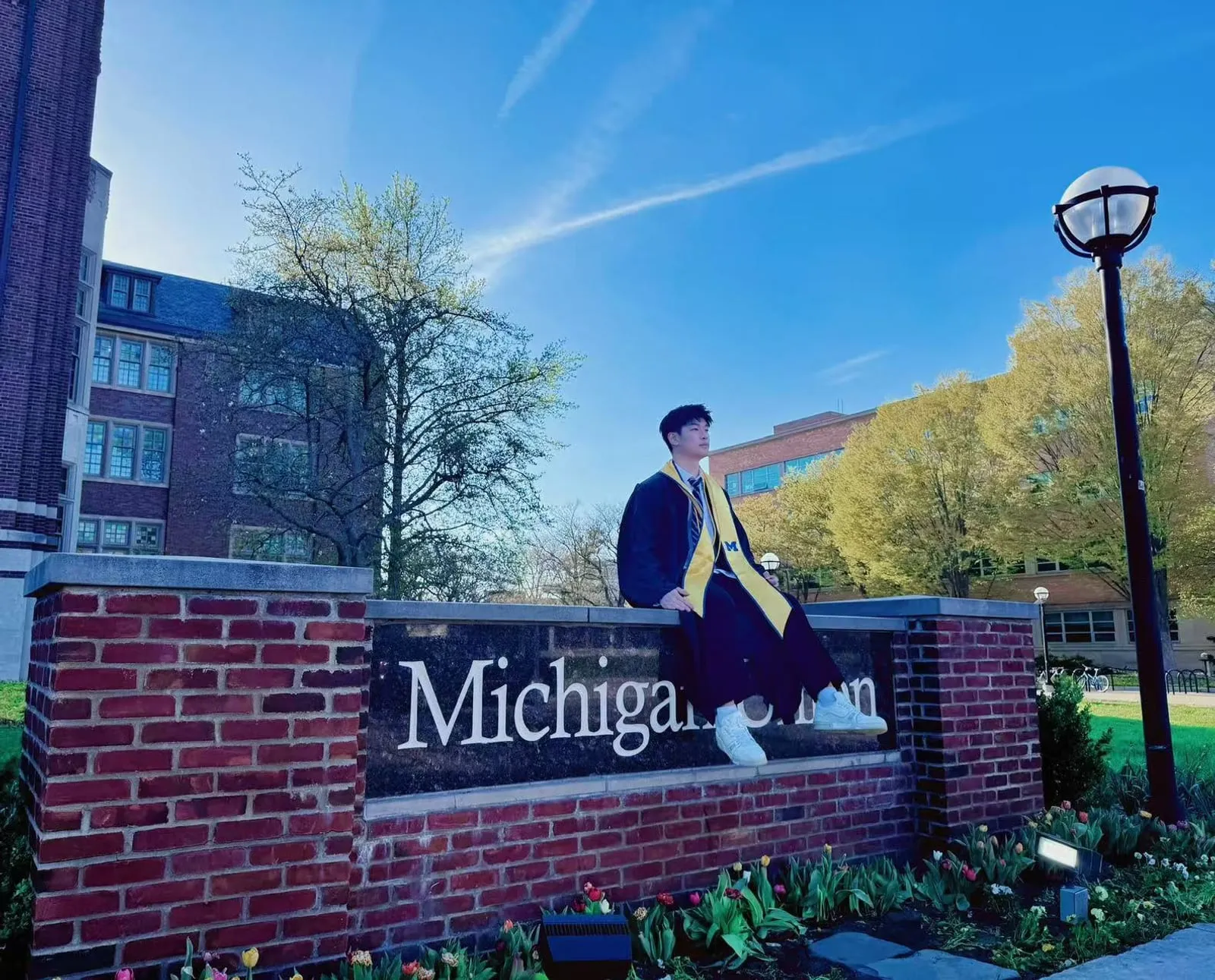 Sitting on the Michigan Union sign in cap and gown, Ann Arbor, May 2025